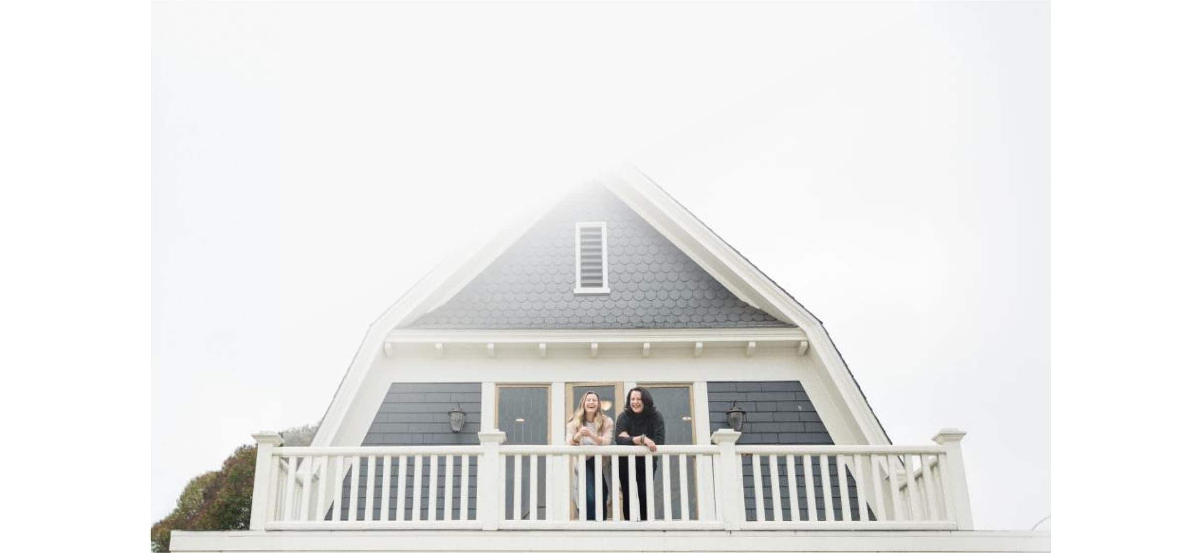 Nicole and Anne standing on a balcony at the top of a house laughing.
